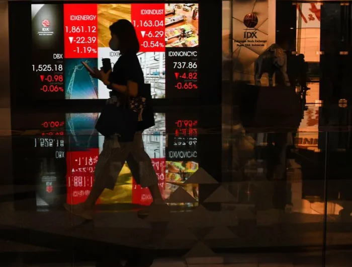 Sumber Foto : katadata, Karyawati berjalan di depan layar digital yang menampilkan pergerakan Indeks Harga Saham Gabungan (IHSG) di Bursa Efek Indonesia (BEI), Jakarta, Rabu (17/5/2023).