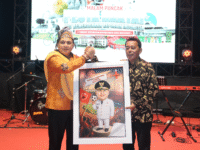 Sumber Foto : Humas Pemkot, Wali Kota Makassar, Munafri Arifuddin, menerima karikatur bertema Stadion Internasional Untia saat malam puncak pesta rakyat Kecamatan Biringkanaya, Selasa (26/8/2025) malam.